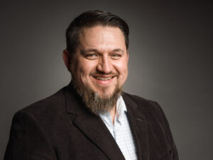 Freundliches Business-Porträt eines Mannes vor dunklem Hintergrund.