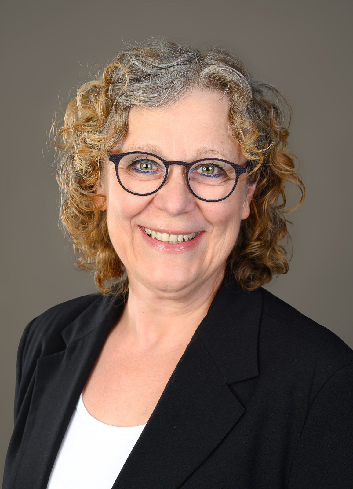 Freundliches Business-Porträt einer Frau vor neutralem Hintergrund.