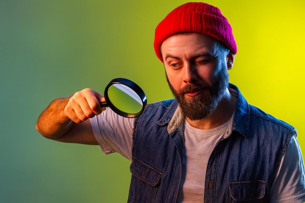 Mann mit roter Mütze betrachtet durch eine Lupe ein Bild – Symbol für den Bild-Check im Fotostudio Donauwörth